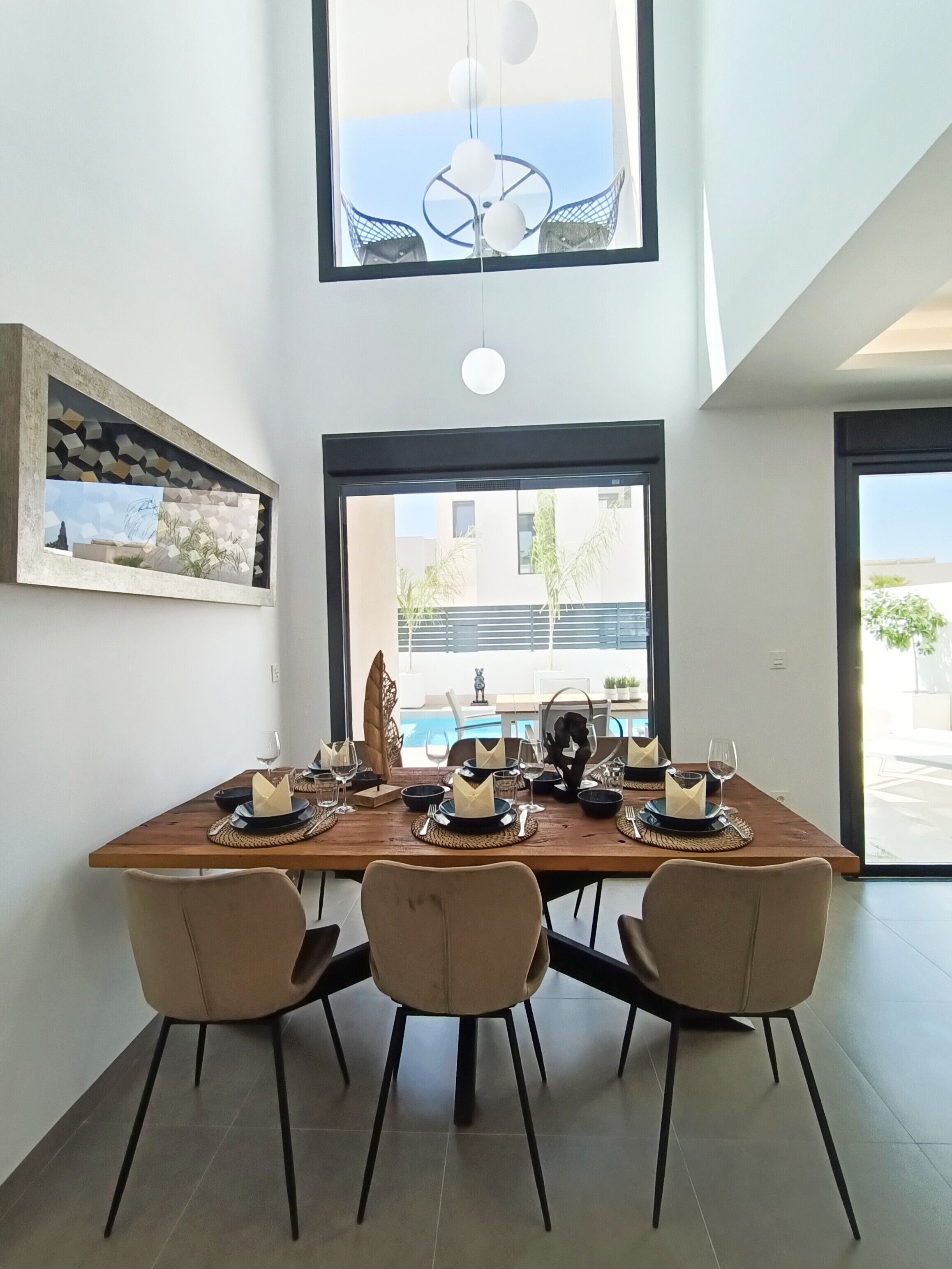 Een eetgedeelte met een houten tafel voor vier personen, stoelen en uitzicht op een zwembad door grote ramen.