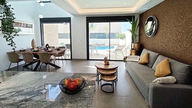 Een moderne woonkamer met een eethoek en uitzicht op een zwembad, met een grijze bank.