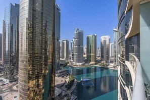 A high-rise building with a curved glass facade, a waterfront with a boat dock, and other modern skyscrapers in the background. - StayShort - Bright 1BR in JLT with Stunning Lake Views! (Dubai)