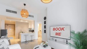 A modern hotel room with a dining area, a kitchen, and a 'BOOK ME' sign. - StayShort - Bright 1BR in JLT with Stunning Lake Views! (Dubai)