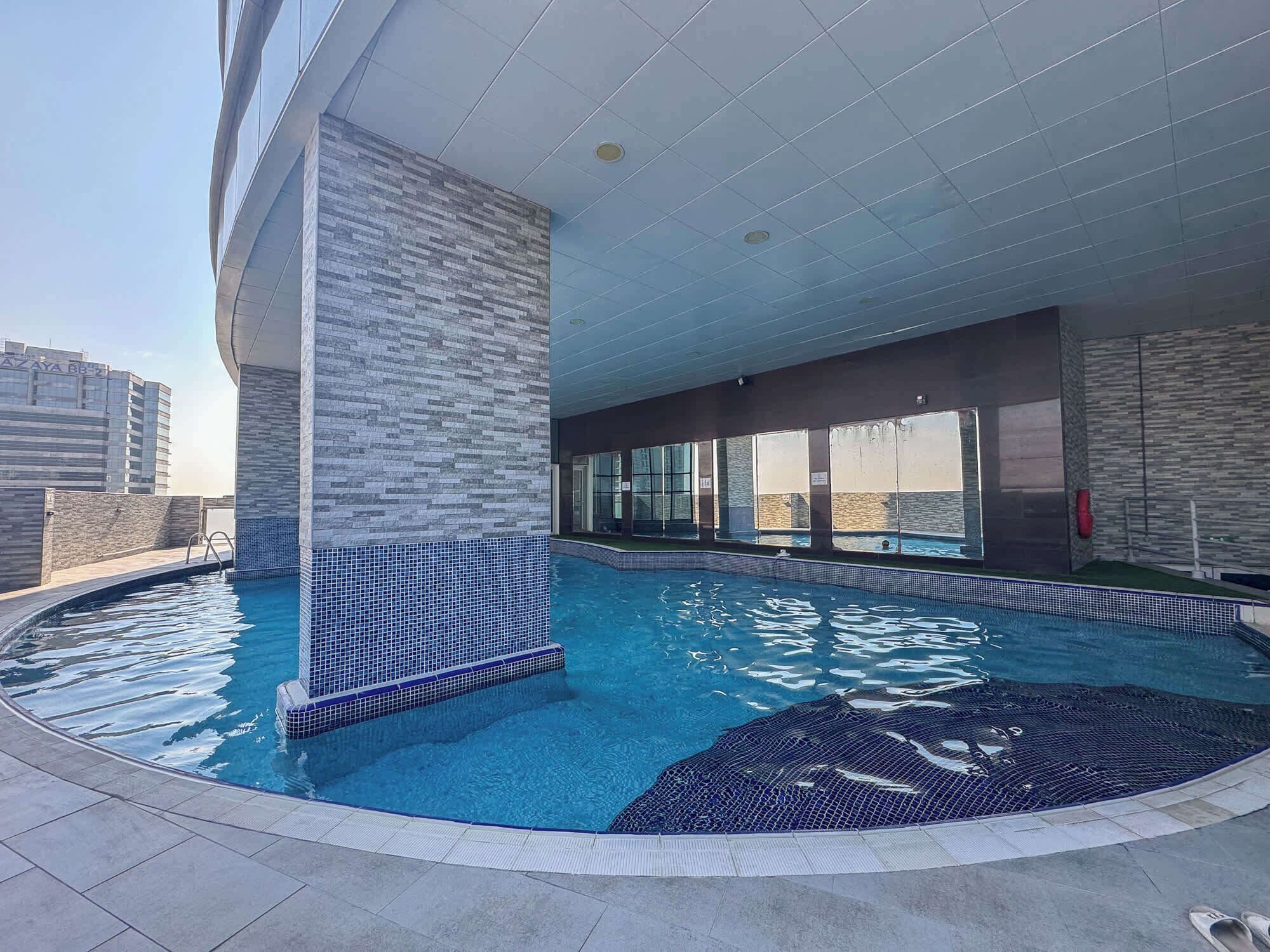 A rooftop swimming pool with a tiled edge, large windows, and a view of the city skyline.
