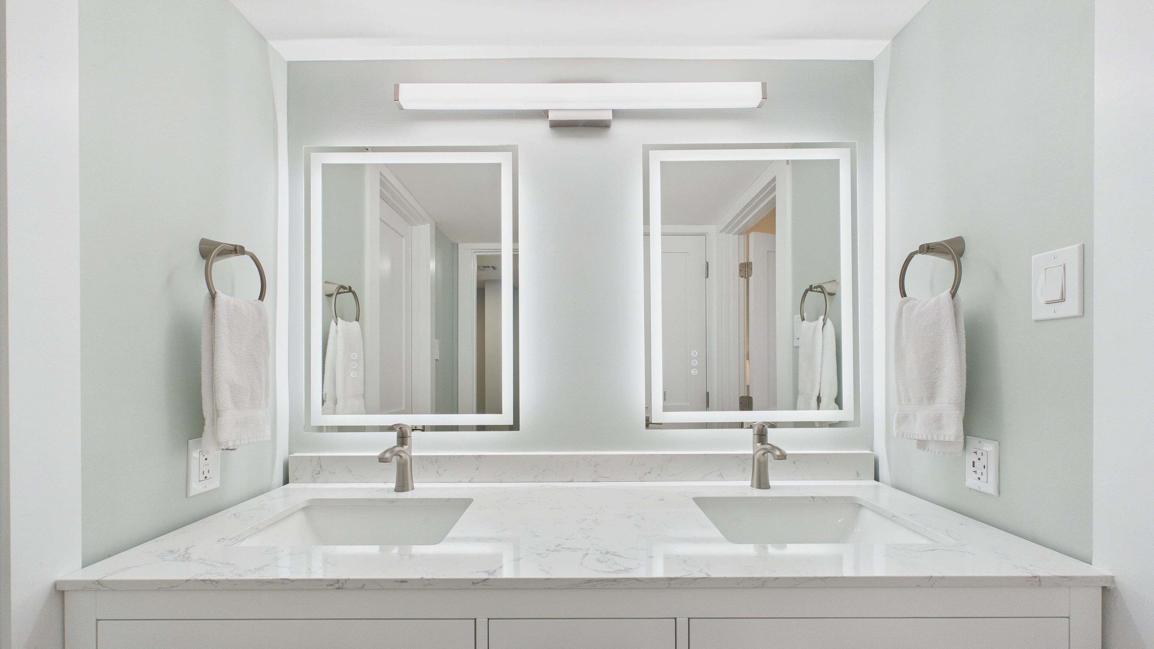 Un bagno con due lavabi, uno specchio grande e un lampadario sopra.