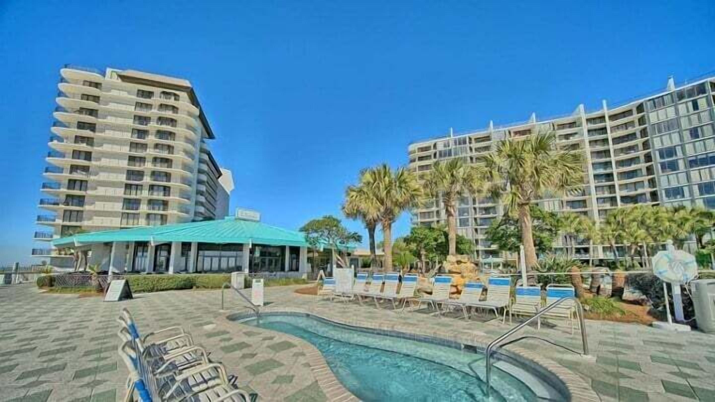 A hotel with a swimming pool, lounge chairs, and palm trees.