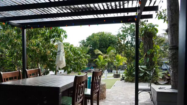 Une terrasse extérieure avec une table et des chaises, entourée de verdure et agrémentée d’une pergola.