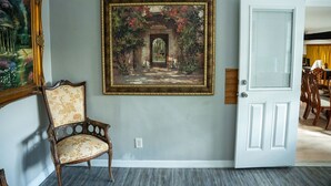 Un couloir orné d’un tableau encadré représentant un jardin, avec une chaise en bois et une porte blanche.