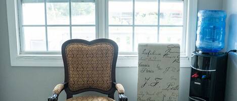 Une pièce dotée d’une grande fenêtre, d’un plancher en bois, d’un fauteuil ancien et d’un distributeur d’eau.