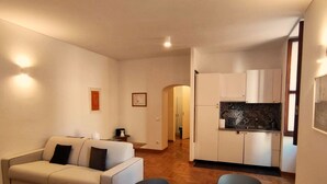 Ein Wohnzimmer mit einer Couch, einem Esstisch und einer Küchenzeile mit Schränken und einer Arbeitsfläche.