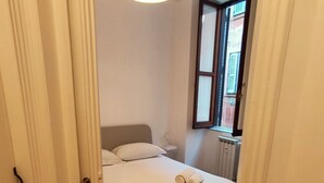 Ein Schlafzimmer mit Holzboden, einem Bett mit weißer Bettwäsche, einer Nachttischlampe und einem Fenster mit Rollläden.