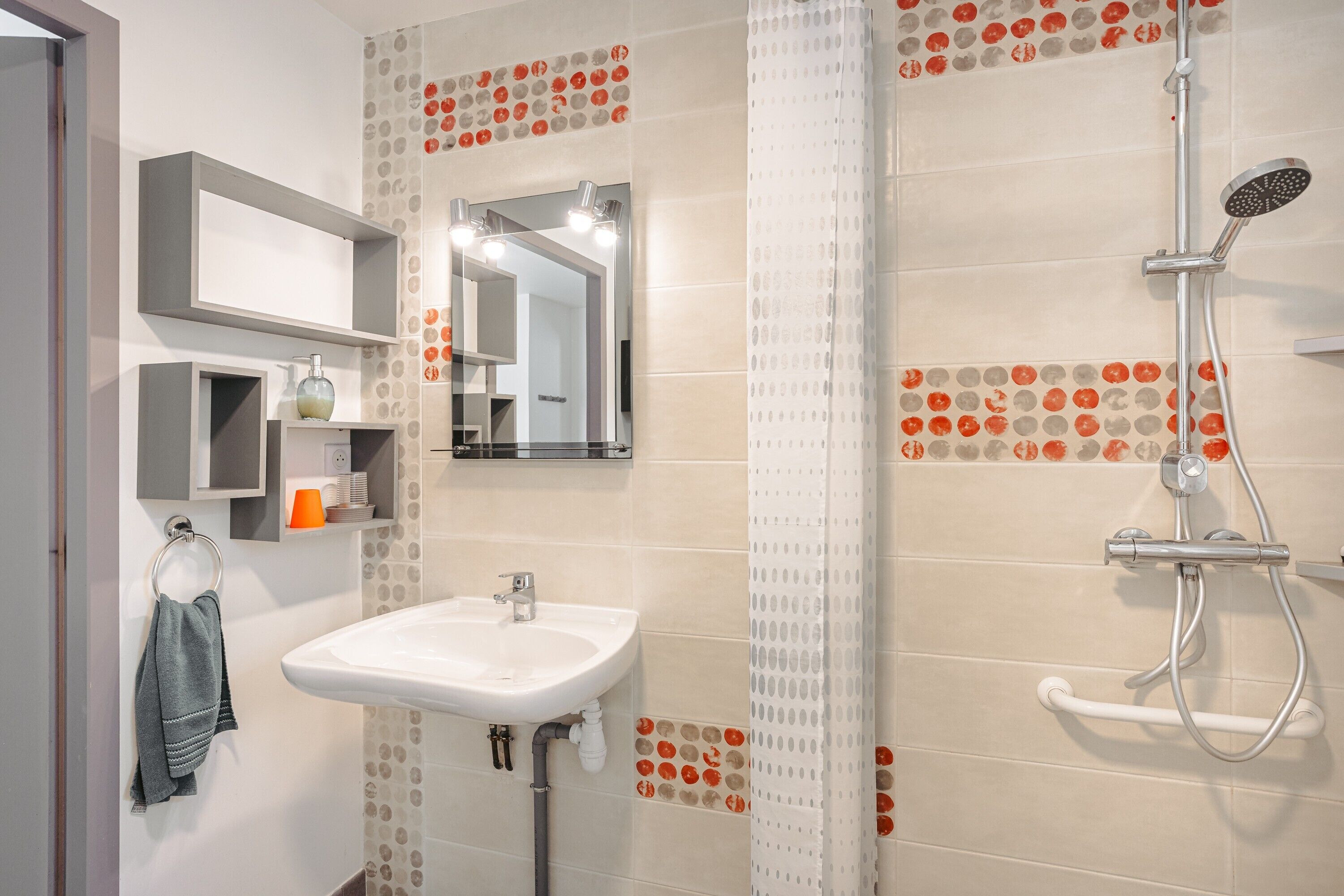 Une salle de bain avec un lavabo, un miroir, une douche et des carreaux décorés.
