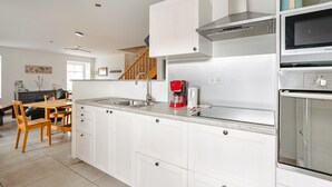 A modern kitchen with white cabinets, stainless steel appliances, and a dining area with wooden chairs. - Gîte du Maroye with Pool (Montreuil)