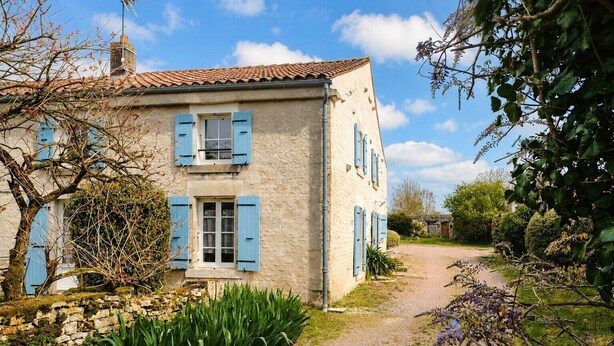 A two-story house with blue shutters, a stone wall, and a gravel path leading to the entrance. - Gîte du Maroye with Pool (Montreuil)