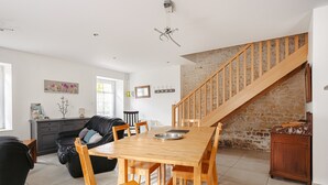 A spacious living area with a wooden dining table, black leather sofa, and a staircase with a stone wall. - Gîte du Maroye with Pool (Montreuil)