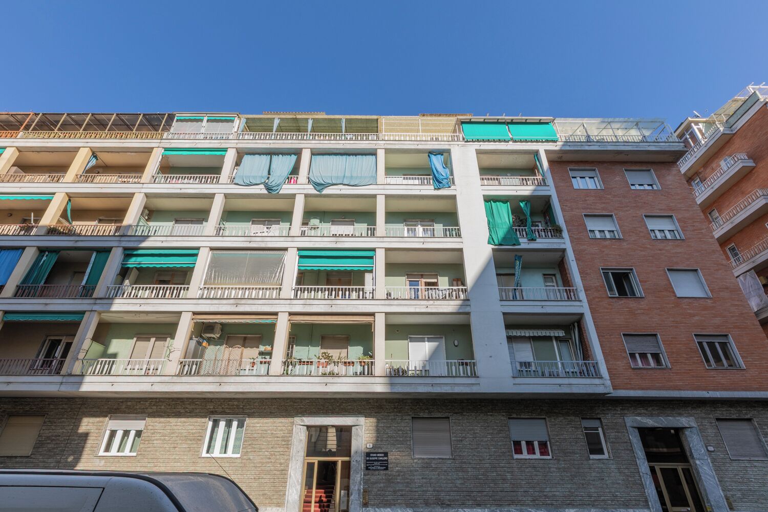 Un immeuble résidentiel à plusieurs étages, doté de balcons, d’une entrée au niveau du sol et d’une enseigne bien visible indiquant la présence d’un commerce au rez-de-chaussée.