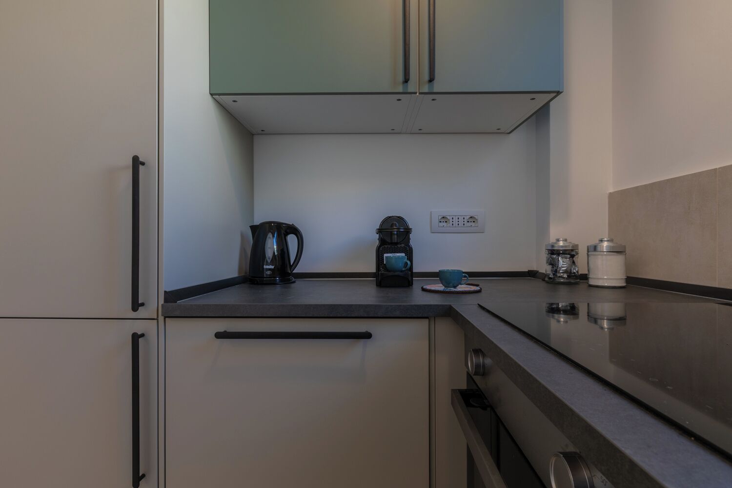 A modern kitchen with a black countertop, a kettle, a coffee maker, and a water dispenser.