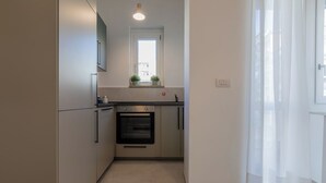 A compact kitchen with a built-in oven, a window above the sink, and a door leading to another room. - Tripoli White Home by Wonderful Italy (Turin)