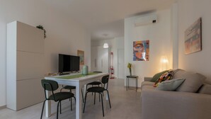 A modern living room with a sofa, a dining table with chairs, a flat-screen TV, and artwork on the walls. - Tripoli White Home by Wonderful Italy (Turin)