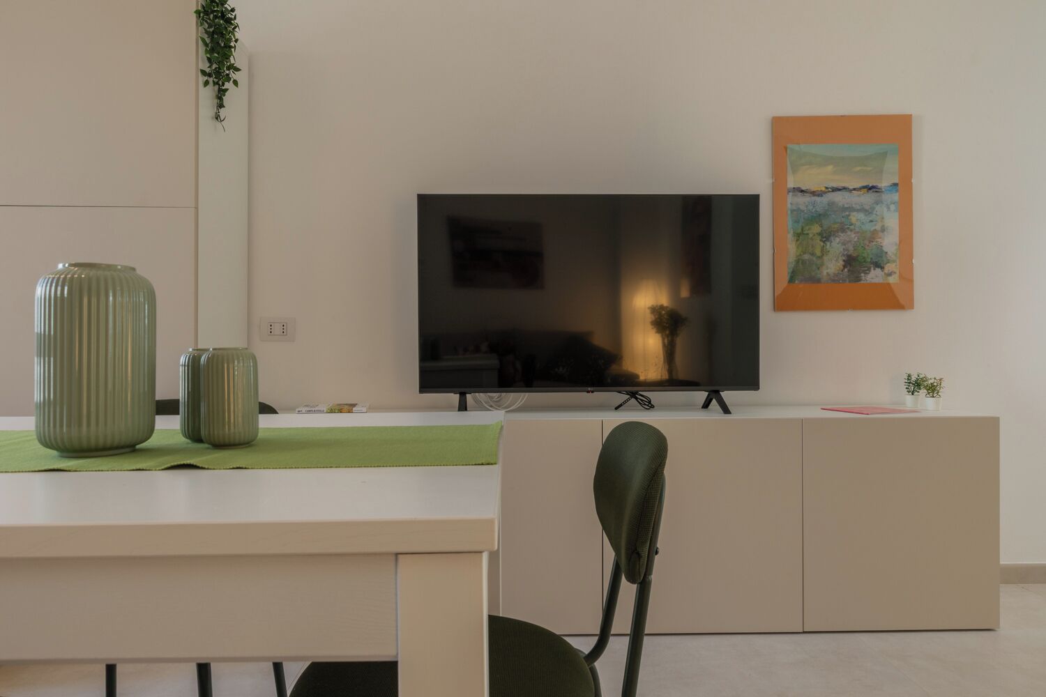 A modern living room with a flat-screen TV, a painting, and a green plant.