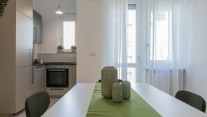 A modern kitchen with white cabinets, a built-in oven, and a dining area with a white table and green runner. - Tripoli White Home by Wonderful Italy (Turin)