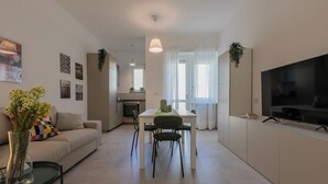 A modern apartment with a living room, dining area, and kitchen. There is a TV on the right side and a dining table with chairs in the center. - Tripoli White Home by Wonderful Italy (Turin)