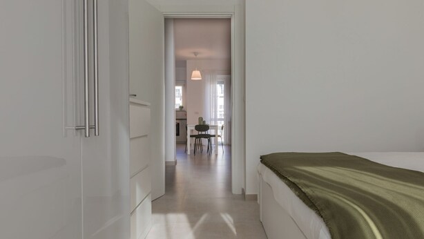 A bedroom with a bed, a green throw, and a hallway leading to a dining area. - Tripoli White Home by Wonderful Italy (Turin)
