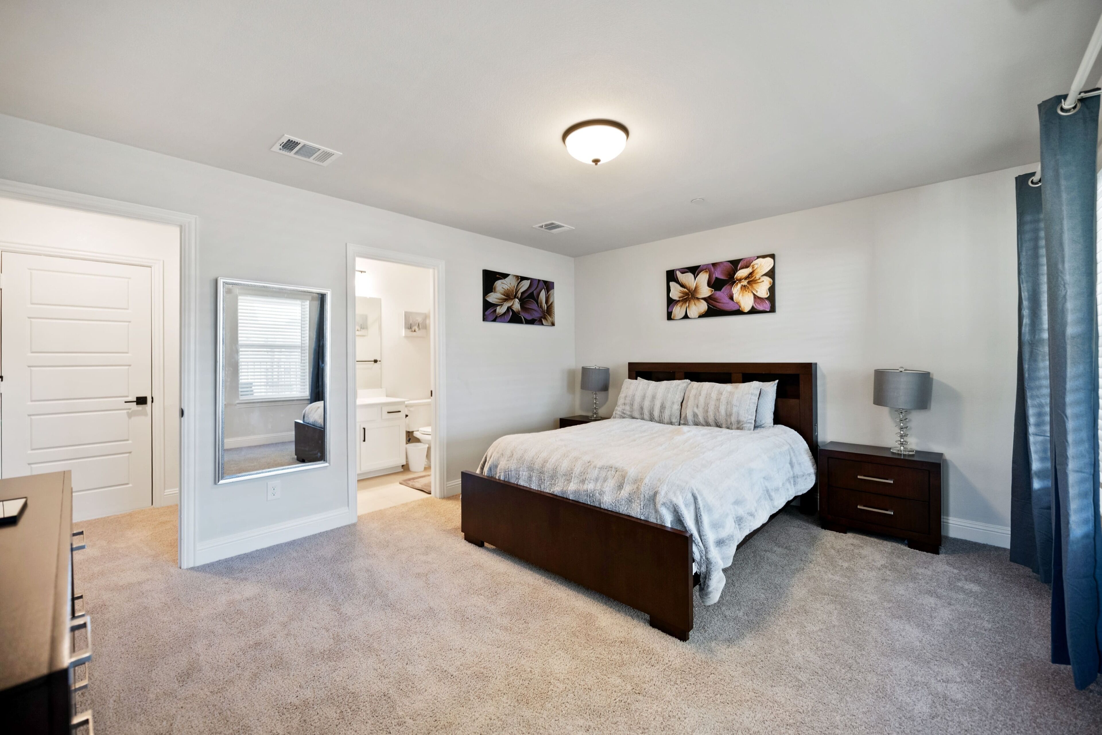 A bedroom with a bed, bedside tables, a mirror, and a door.