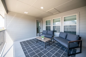 A covered porch with a sofa and a table, a door, and a window with blinds. - PL088 - Home|Yard|16mi to Convention Ctr|Sleeps 8 (Plano)