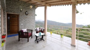 A covered balcony with a stone wall, wooden furniture, and potted plants. - THE MOKSH ECO INN (Dhari)