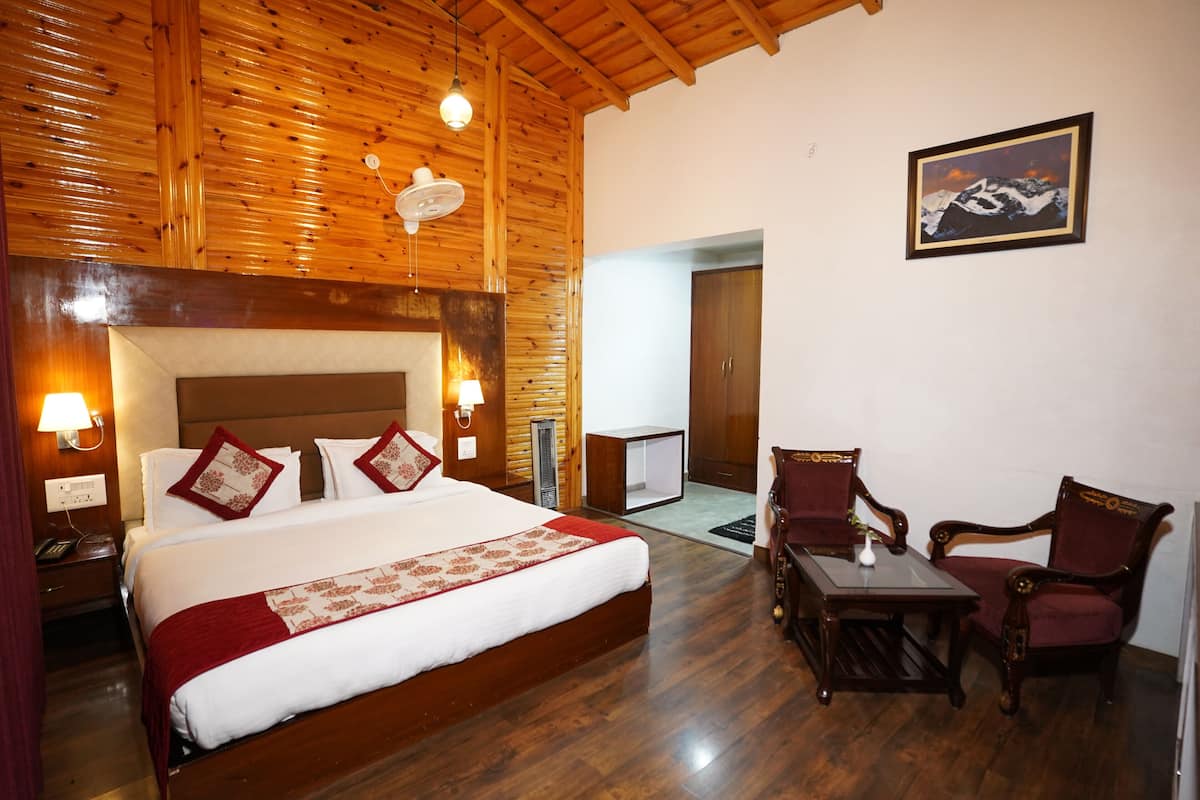 A hotel room with a wooden ceiling, a large bed with red and white bedding, two chairs, a table, and a framed picture on the wall.