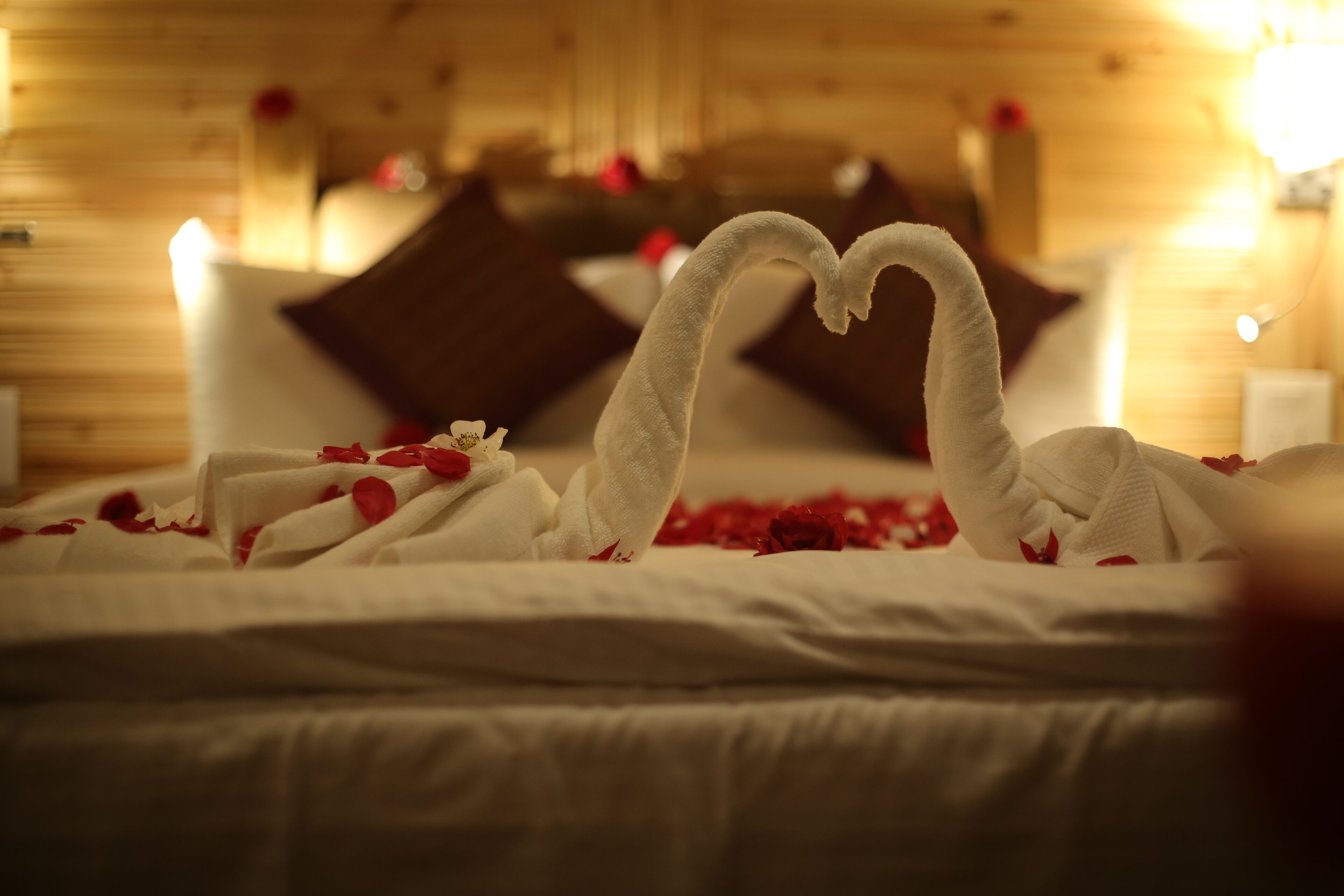 A bed with a heart-shaped towel arrangement and rose petals.