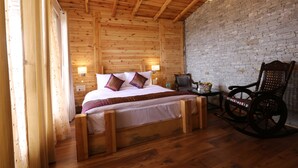 A wooden room with a bed, a rocking chair, and a brick wall. - THE MOKSH ECO INN (Dhari)