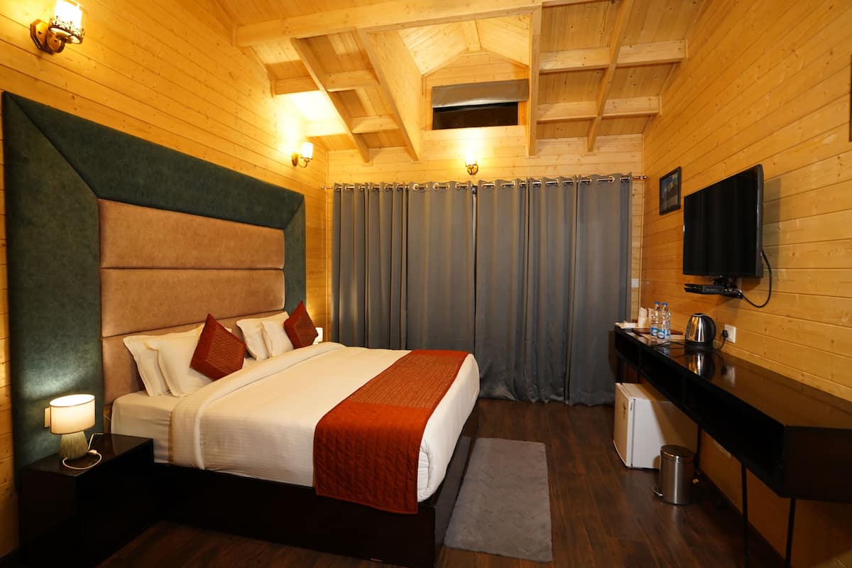 A hotel room with a large bed, a desk, a television, and a small refrigerator.
