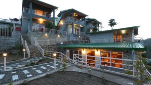 A multi-story stone building with a green roof, multiple balconies, and a well-lit interior. - THE MOKSH ECO INN (Dhari)