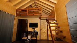 A wooden interior with a loft bed, a desk with chairs, a television, and a ladder. - THE MOKSH ECO INN (Dhari)