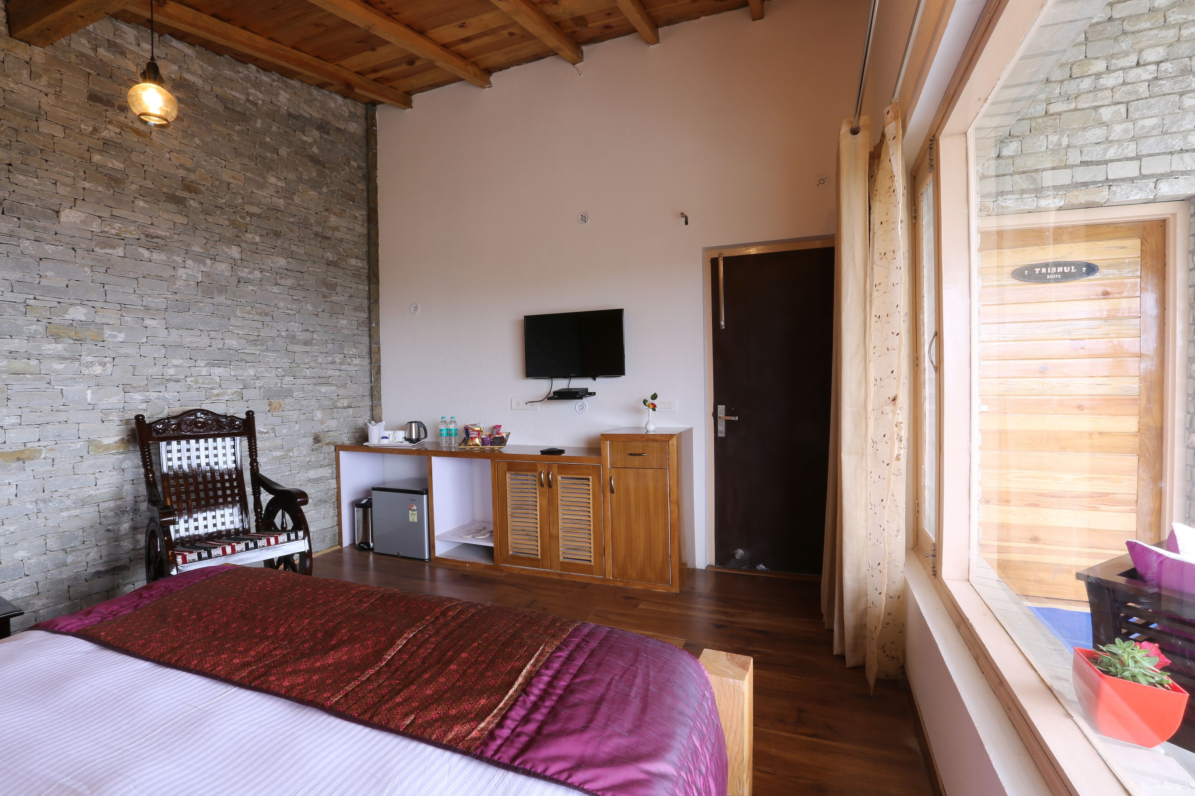 Un dormitorio con cama, escritorio, televisión y ventana con cortinas.