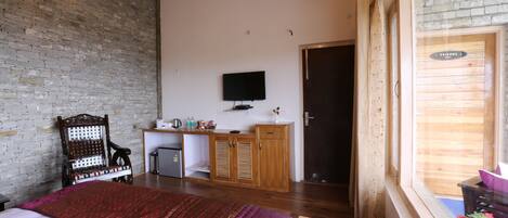 Un dormitorio con cama, escritorio, televisión y ventana con cortinas.