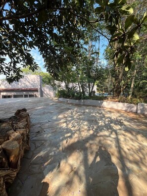 A paved courtyard with stone walls and trees providing shade. - 4-bedroom Retreat With Lush Gardens Pool- 2346 (Harare)