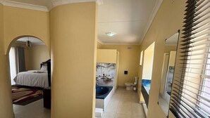 A hotel corridor with a bed, a bathroom, and a dining area. - 4-bedroom Retreat With Lush Gardens Pool- 2346 (Harare)