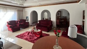 A spacious living room with red sofas, a wooden coffee table, and a chandelier. - 4-bedroom Retreat With Lush Gardens Pool- 2346 (Harare)
