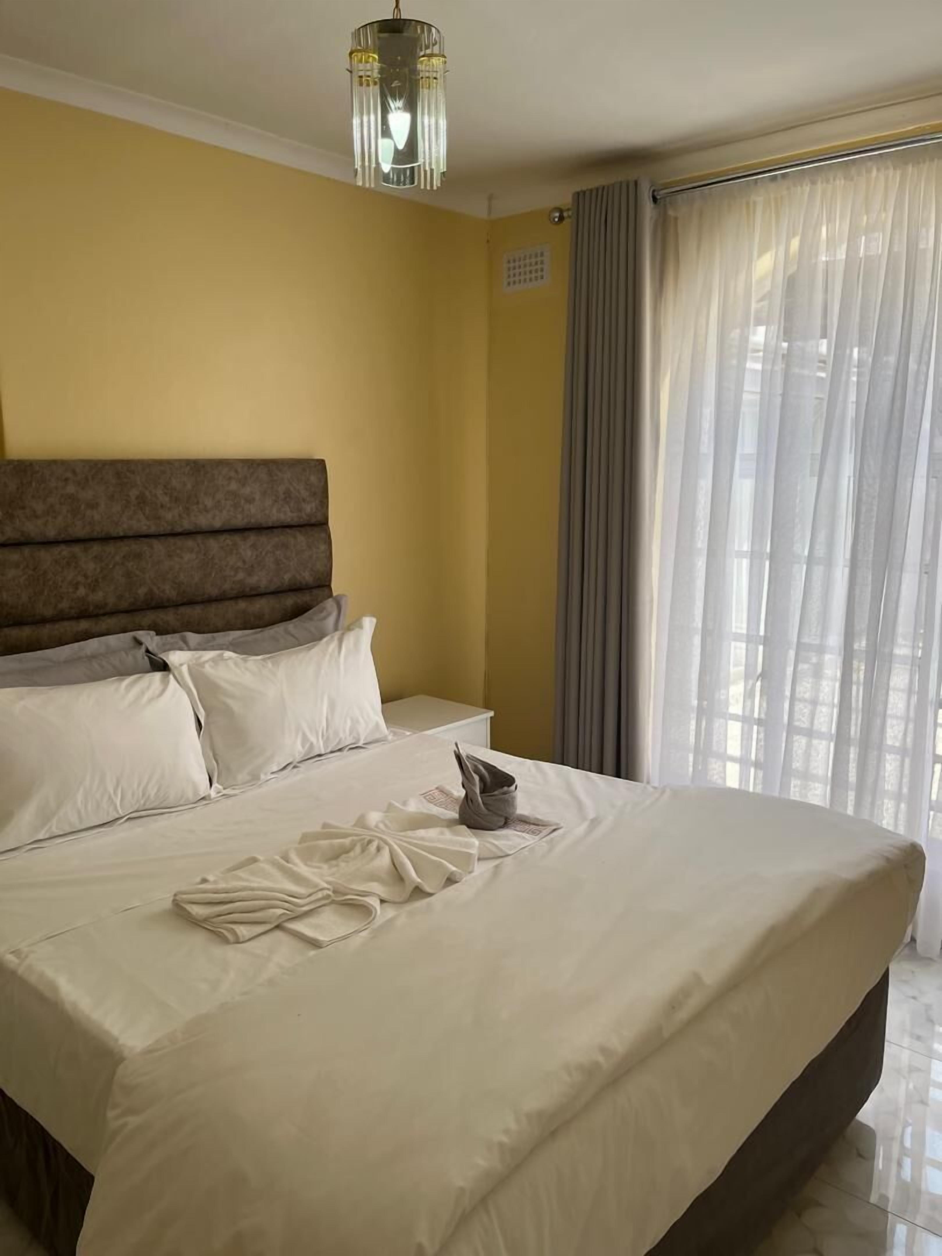A hotel room with a large bed, a headboard, a bedside table, and a window with curtains.