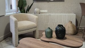 Un salon avec un téléviseur à écran plat fixé au mur, un fauteuil beige, une table basse en bois et un tapis à motifs.