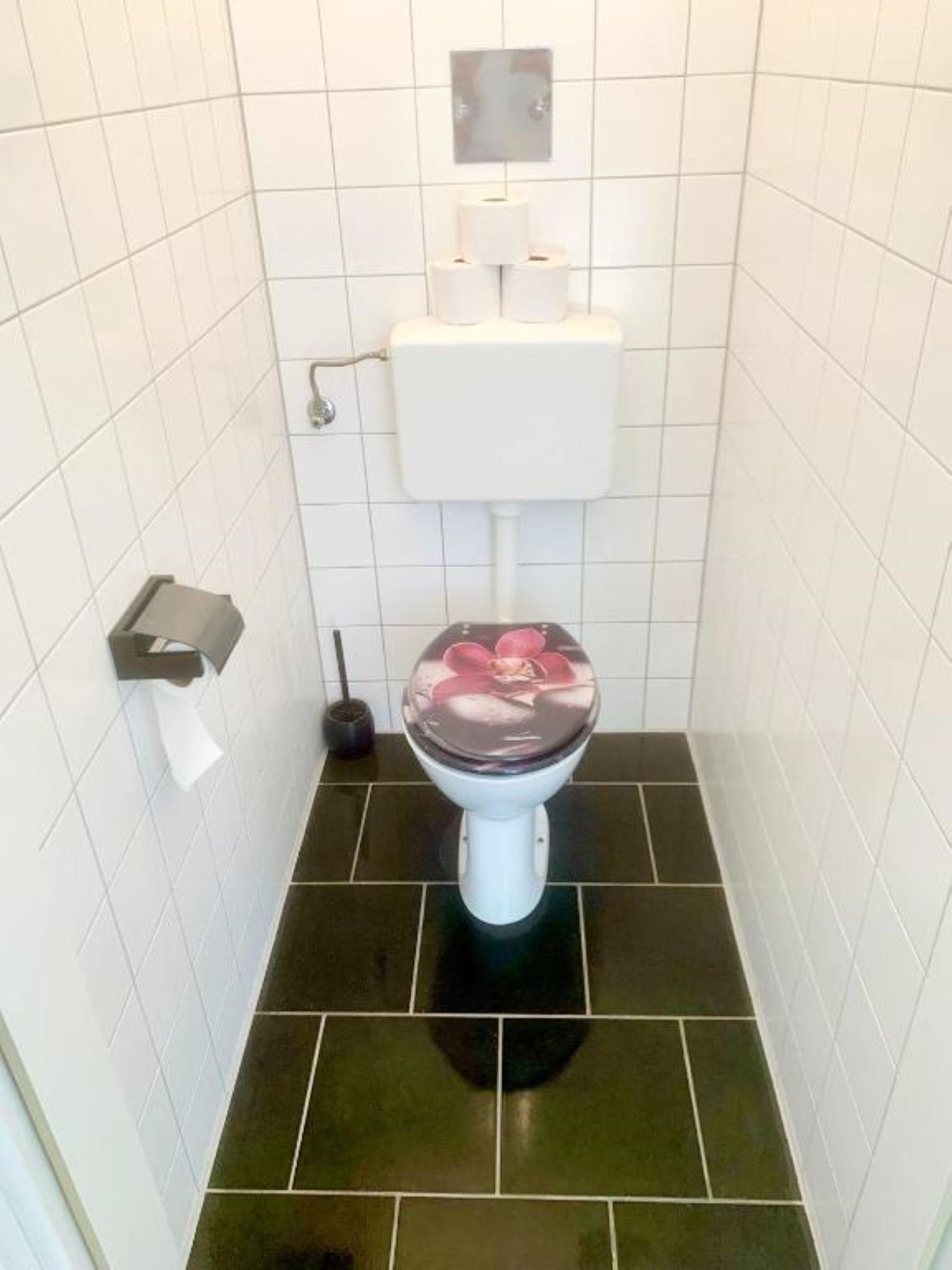 A bathroom with a white toilet, black floor tiles, and white tiled walls.
