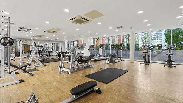 A gym with various exercise equipment, large windows, and a wooden floor. - O2 & ExCeL! Modern 1 Bed Flat + Sofa Bed • Ideal for Conferences & Families (London)