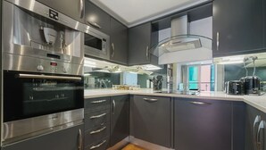 A modern kitchen with stainless steel appliances, dark cabinetry, and a wooden floor. - O2 & ExCeL! Modern 1 Bed Flat + Sofa Bed • Ideal for Conferences & Families (London)