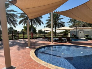 A pool area with lounge chairs and umbrellas, surrounded by palm trees and a tiled walkway. - 4 Beds Townhouse in Redwood Jumeirah Golf Estates (Dubai)