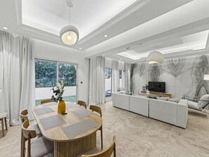 A modern living room with a dining area, a sofa set, and a TV. - 4 Beds Townhouse in Redwood Jumeirah Golf Estates (Dubai)