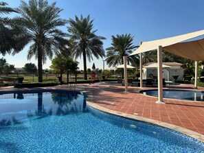 A swimming pool with a tiled edge, surrounded by palm trees and a covered seating area. - 4 Beds Townhouse in Redwood Jumeirah Golf Estates (Dubai)