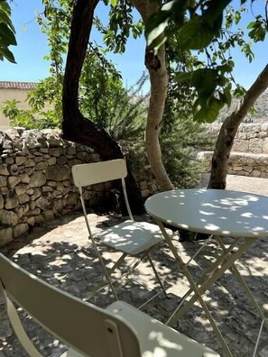 An outdoor seating area with a table and chairs under trees. - The Stone Crow Corto Maltese (SCICLI)
