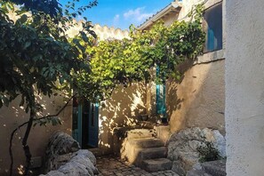 Une cour étroite, avec des marches en pierre menant à une porte, le tout entouré de murs et de végétation.