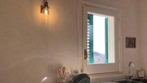 Une cuisine équipée d’une cuisinière à gaz, d’un évier, d’une fenêtre avec stores, d’un luminaire fixé au mur et d’un porte-assiettes décoratif.