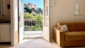 Une chambre avec balcon, un canapé, un coin cuisine et vue sur un bâtiment historique.
